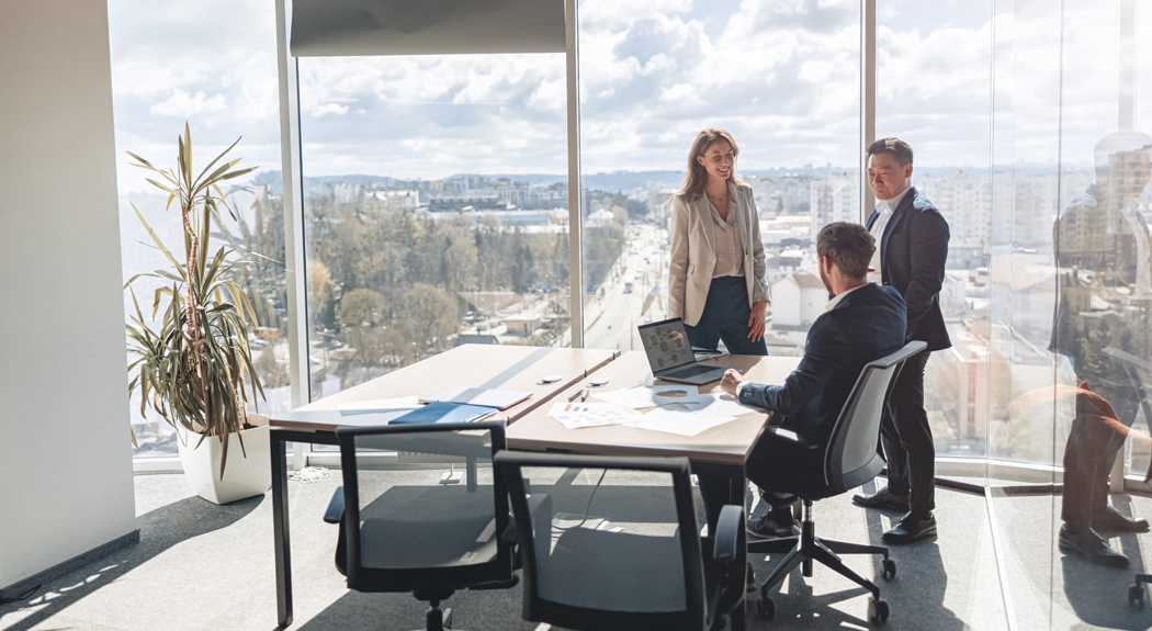Ein sonniges Büro in einem hohen Stockwerk, und das Team hat eine lockere Besprechung.