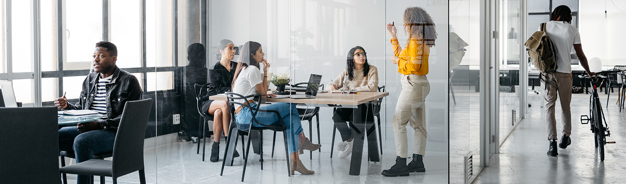 Das Team hält eine Besprechung in dem transparenten Besprechungsraum ab, während der Raum mit Menschen gefüllt ist.