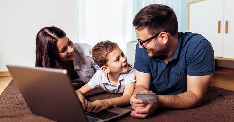 Schöne Eltern und ihr Sohn kaufen online ein, indem sie einen Laptop benutzen und zu Hause lächeln