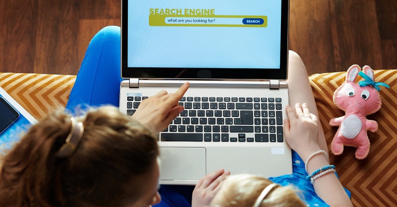 Mother teaching daughter how to use search engine on laptop
