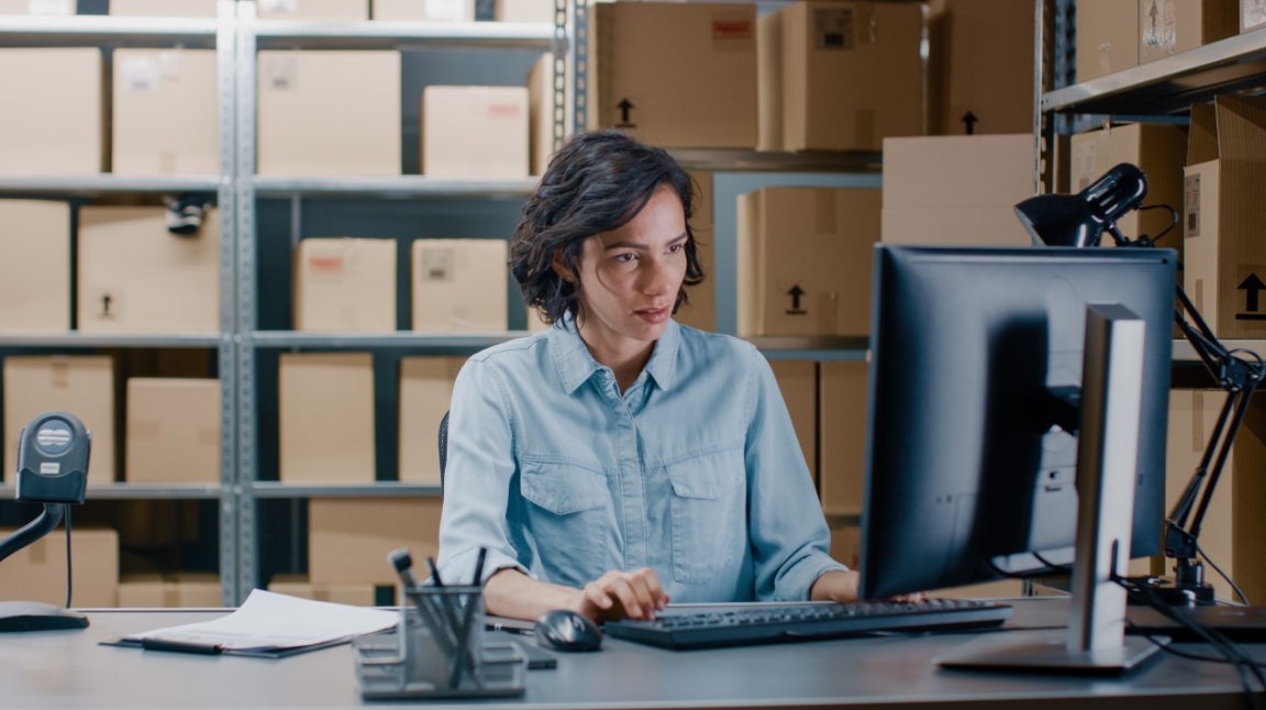 Woman sitting in fron tof a computer at a warehouse