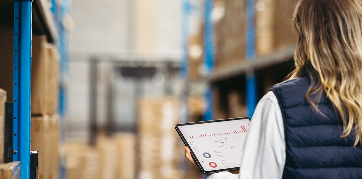 Woman in a warehouse, checking her tablet with ecommerce services on